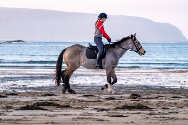 BURTONPORT, İLK DONEGAL, IRELAND - 18 ARALIK 2021: Patricia Ward sahilde atına biniyor