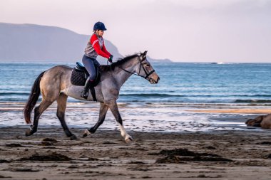 BURTONPORT, İLK DONEGAL, IRELAND - 18 ARALIK 2021: Patricia Ward sahilde atına biniyor