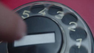 Telefon ahizesini kaldıran ve eski kırmızı bir pervanenin numarasını çeviren elin yakın görüntüsü.