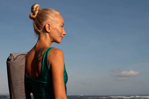 Güzel bir kız yoga minderiyle sahilde yürüyor. — Stok fotoğraf