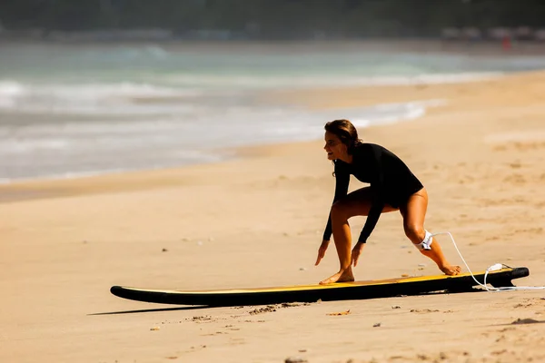 beautiful girl get up on a surfboard on the sand