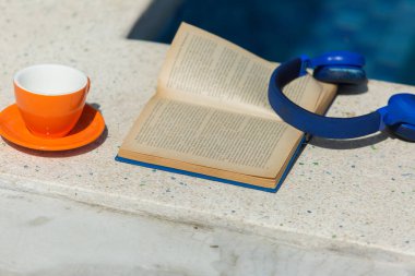 Turuncu bardak, kitap, yüzme havuzunun yanında mavi kulaklık. Yüksek kalite fotoğraf