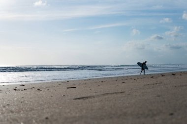 Kuta plajı boyunca yürüyen sörfçü. bali