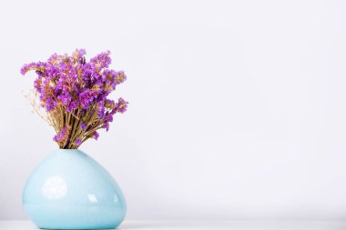 Mavi bir vazoda, beyaz bir arkaplanda, bir buket menekşe çiçeği..