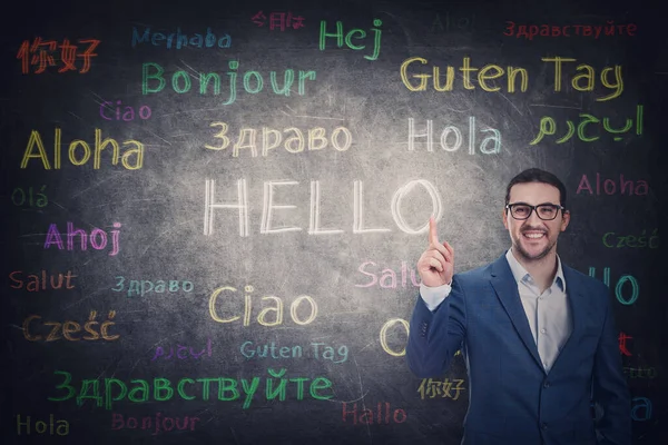 Confident businessman knows different languages. Person shows index finger to the blackboard with word hello translated in multiple foreign languages. Business learning concept