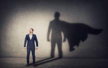 Kararlı iş adamı kahraman duruşuna güveniyor ve arkasında cesur bir süper kahraman gölgesi bırakıyor. İş liderliği ve motivasyon kavramı. Hırs ve güç sembolleri