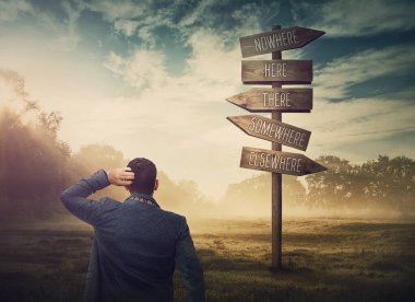 Kaybolmuş ve kafası karışmış bir işadamı imkansız yönler gösteren bir tabelanın önünde. İş ikilemi ve zor seçim konsepti. Yol işaretinde doğru yolu seçiyorum.