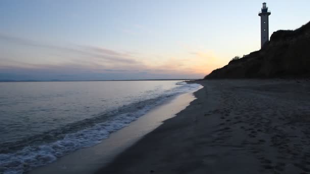 Pôr do sol na praia rochosa e farol — Vídeo de Stock