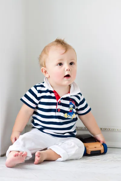 Niño pequeño sentado en el suelo con una máquina de juguete — Foto de Stock