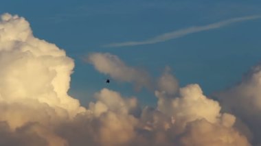 Black small helicopter flying above beautiful sunset cumulus clouds and blue sky