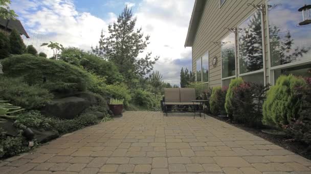 Achtertuin beton bestratingsafwerkmachines patio met bomen, planten, zweefvliegtuig, ingemaakte plant, witte wolken en blauwe hemel venster reflectie timelapse verplaatsen — Stockvideo