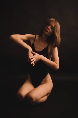 Yerde soyut pozlar, klasik beden kıyafetli bir kız sezgisel olarak siyah arka planda dans ediyor, bulanık fotoğraflar ve bulanık resimler, resim sesleri, odaklanmamış tam boy portreler.