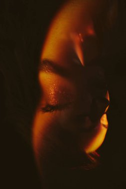 Kadın yüzü ve sıcak bir ışık bulanıklığı, siyah arka planda bir sanat modası portresi. Yakın planda bir kadının bulanık ve odaksız portresi