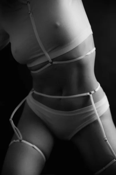 fashion portrait of a girl in white underwear and a belt on black background. Fine art photo of female body.