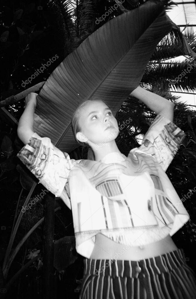 Fashion portrait of a girl in fashionable clothes on black and white grainy film in the botanical garden. Fashionable effects of blurring, defocus and fuzziness of the film image. Stylish frame for a magazine