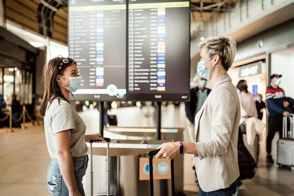 Two Travelling Women Wearing Protective Masks Discussing Flight Information Board — Stock Photo, Image