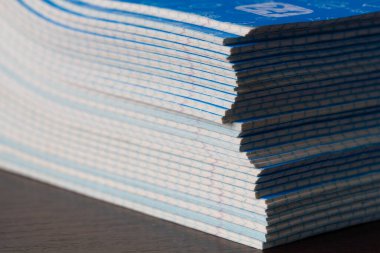 Defterler yığını. Sınıftaki kahverengi masanın üzerinde bir paket mavi okul not defteri. Bir yığın egzersiz kitabı. Kurallı kağıt. Anaokulu eğitimi için kareli matematik defterleri paketliyorum. Yakın plan.