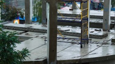Yağmurda inşaat alanında. İnşaatçılar kötü hava koşulları nedeniyle işyerinden ayrıldılar. Beton levhalar ve önceden hazırlanmış beton yığınları suyla doludur. İşçiler zorla mola verdiler.
