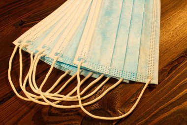 Kahverengi ahşap bir masada tek kullanımlık mavi yüz maskeleri. Güzel ahşap desenli arka planda bir sürü cerrahi 3 katlı maske var. Hijyen ve sağlık. Yeni bir Coronavirus türüne karşı koruma