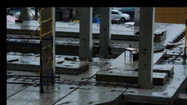 Yağmurda inşaat alanında. İnşaatçılar kötü hava koşulları nedeniyle işyerinden ayrıldılar. Beton levhalar ve önceden hazırlanmış beton yığınları suyla doludur. İşçiler zorla mola verdiler.
