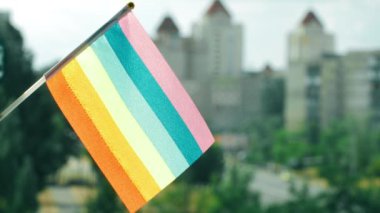 LGBTQ bayrağı mavi gökyüzüne ve şehir caddesine dikildi. LGBTQIA bayrağı dalgalanıyor. Renkli LGBT bayrağında gökkuşağı çizgileri. LGBTQI + 'nın güneş bayrağı. Şehrin sokakları. Metin için alanı kopyala