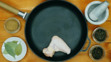 The cook puts the chicken wings in the pan. Chicken wings in a cast iron skillet ready to marinate. Black peppercorns, dried cloves, mustard, bay leaf and spices. Meat in a pan. Close-up. Top view
