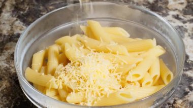 Grated cheese falling on plate with Italian penne rigate pasta. Cheese fell in the deep transparent plate with pasta feathers. Tubular pasta. Traditional Cuisine. Durum wheat pasta. Food background