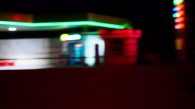Arabanın camından gece şehrinin bulanık görüntüsü. Parlak renkli ışıkları olan güzel hareketli bir arka plan. Akşam sokakları, aydınlık otoyollar, reklam tabelaları, alışveriş merkezleri ve benzin istasyonları