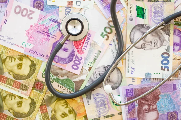 Stethoscope and money. The concept of expensive medicine. Ukrainian hryvnia. Lots of banknotes on the table. A lot of money on the background. Health care. Expensive Medication. Close-up. Top view