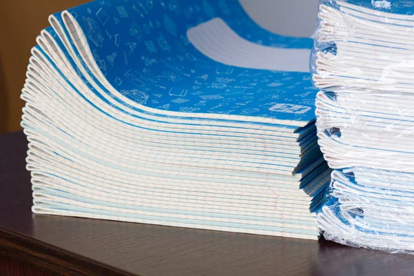 Stack of Notebooks. Back to school. A pack of blue school notebooks on the table in a classroom. Stack of exercise books. Packing checkered math notebooks for preschool education. Class room. Close-up