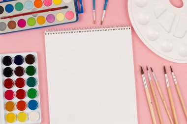 Okula dönelim. Fırçalar, boyalar ve paletler masanın üzerinde. Farklı boyutlarda fırçalar, güzel pembe bir arka plan çizmek için çok renkli parlak boyalar. Metin için boşluk. Üst görünüm