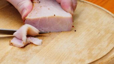 The chef cuts the ham. A man cuts fresh homemade smoked pork ham on a wooden table. Cooked piece of meat on a cutting board. Close-up. Concept of delicious food snacks and cooking. Copy space for text