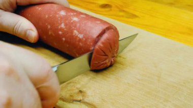 Cutting sausage on wooden chopping board. The cook cuts the sausage into pieces on a wooden cutting board. Beautiful homemade salami. Cooking sandwiches in the kitchen. Healthy food. Close-up