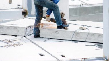 Profesyonel bir inşaatçı inşaat sahasında güçlendirilmiş beton levha ile demir demiri öğütücü ile keser. Elektrikli testereden kıvılcımlar uçuşur. Yeni bir binanın inşaatı.