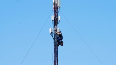 Electrician repairman repairs a mobile communication antenna. Repair work to restore wireless internet and mobile communications at high altitude. Cell tower among blue clouds. Electronic equipment