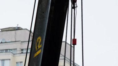 Construction crane. Lifting mechanism, winch, hook and iron ropes against the backdrop of a blue sky and a multi-storey residential building with balconies, conditioners. Construction site equipment