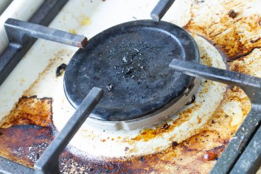 Dirty gas stove surface. Gas burner and cast iron grate of a gas oven surrounded by old leftovers of food and drinks. Top area surface and burner heads needs cleaning from burnt-on grease. Close-up