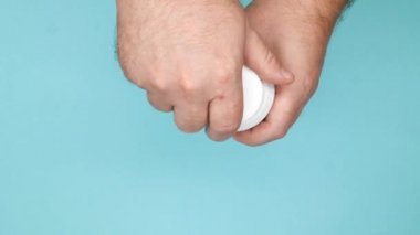 Bir erkek eli tıbbi kapsüllerle şişeyi açar ve avucuna ilaç hapları döker. İlaç şişesinde ve elinde yeşil-beyaz ilaçlar var. Sağlık hizmetleri. Eczane ve tedavi konsepti. Yakın plan. Üst görünüm