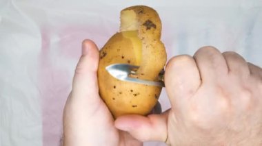 Patates soymak. Patates soyan adamın elleri. Bir adam manuel patates soyucusuyla çiğ patates soyar. Patates soymak ve soymak. Mutfakta yemek pişirmek. Vejetaryen yemeği. Yakın plan. Üst görünüm