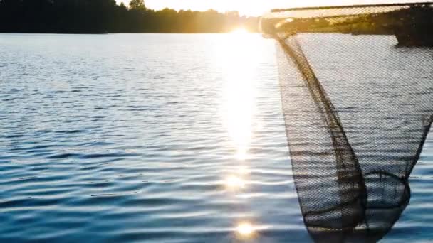 川での日の出と網を持つ漁師 森や船を背景に池の中で穏やかな波 湖の夕日 美しい自然 水の上に太陽の反射 自然の美しさ — ストック動画