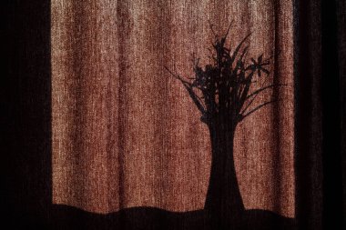 Perdelerinde çiçekler olan bir vazonun gölgesi. Parlak güneşte kahverengi kumaş perdelerin arka planında bir buket çiçekli bir vazonun siyah silueti. Metin için alanı kopyala