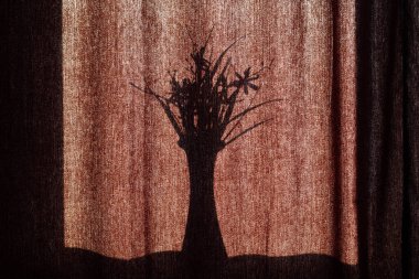 Perdelerinde çiçekler olan bir vazonun gölgesi. Parlak güneşte kahverengi kumaş perdelerin arka planında bir buket çiçekli bir vazonun siyah silueti. Metin için alanı kopyala