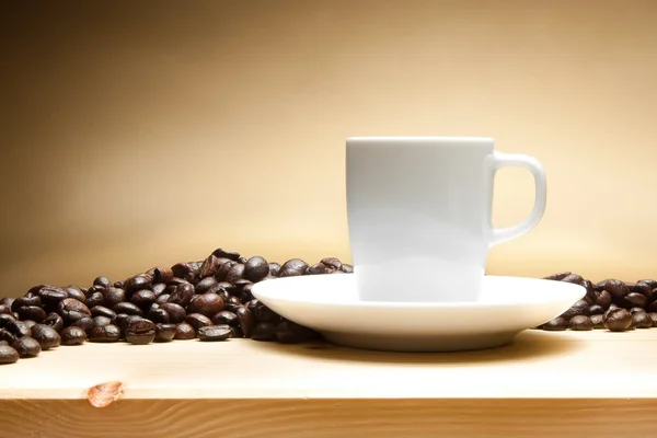 White cup with coffee beans over wood table — Stock Photo, Image