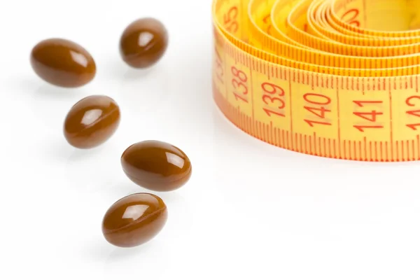 Pilules médicales brunes pour suivre un régime devant un ruban à mesurer — Photo