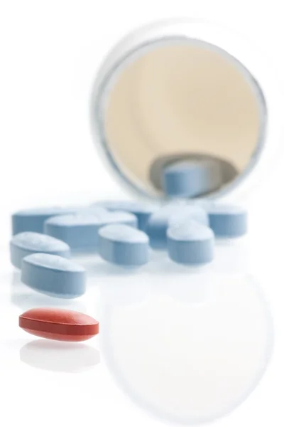 Red medical pill in front of blue pills in laboratory near white container — Stock Photo, Image