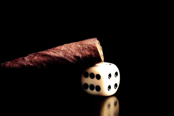 Un dado blanco y un cigarro sobre una vieja mesa marrón de madera —  Fotos de Stock