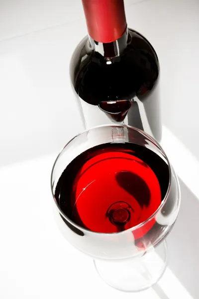 Красный бокал вина рядом с бутылкой при дневном свете — стоковое фото