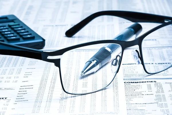 Glasses near calculator with pen on financial newspaper — Stock Photo, Image