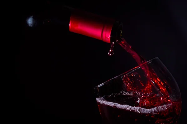 Versando bicchiere di vino rosso sulla luce scura — Foto Stock