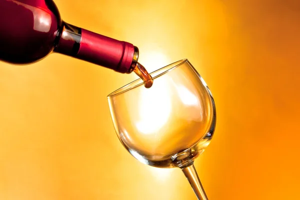 Bottle of red wine beginning filling a glass on golden background — Stock Photo, Image